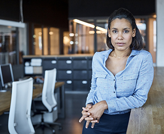 Business woman in office leaning on a table looking into the camera