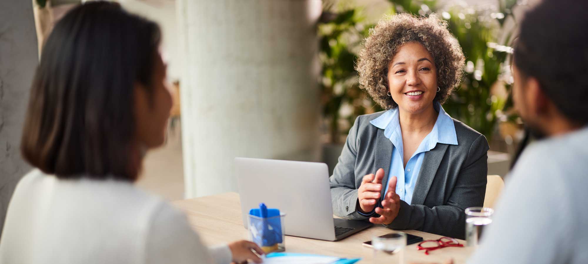 A Western Alliance Bank financial advisor with short curly hair is smiling and gesturing while seated at a table with her computer. She is meeting with a client to discuss their financial needs, symbolizing the expert and personalized service we offer.