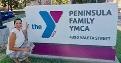 Xochil Sousa stands in front of Peninsula Family YMCA sign