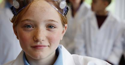 Young girl in a lab coat and googles smirking at the camera