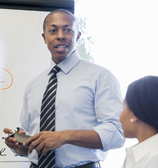 Young businessman smiling while writing on a whiteboard and looking at a business woman