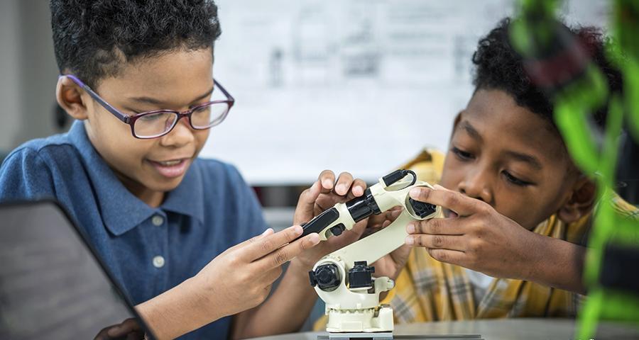 Two elementary school aged kids looking at a small robotic arm