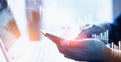 Closeup of a person's hands using a cell phone with a laptop computer in the background