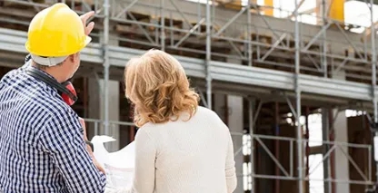 Two people at an industrial construction site looking at plans and the building