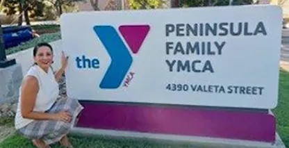 Xochil Sousa stands in front of Peninsula Family YMCA sign