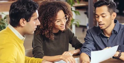 Three young adults looking at a single paper while sitting at a conference room table