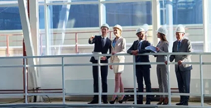 A group of businesspeople wearing hard hats and overlooking a commercial construction site