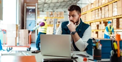 Man sitting at a desk working on a computer in a warehouse.