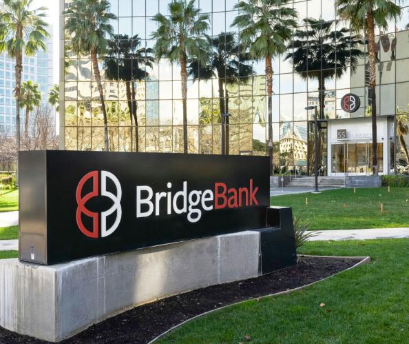 A grass lawn and glass building with the Bridge Bank sign out front