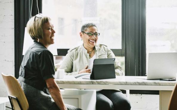 Two women smiling and working on laptops